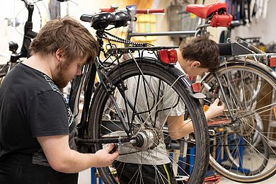 Zwei Jugendliche reparieren Fahrräder, die auf Montageständern befestigt sind