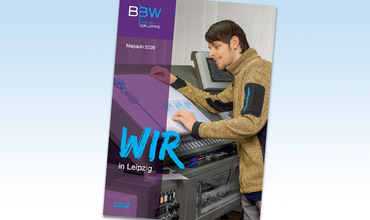 Cover der WIR in Leipzig 2026 - ein junger Mann steht an einer Druckmaschine und betrachtet einen Druckbogen. Er trägt eine beige-melierte Fleecejacke und hat dunkle Haare.