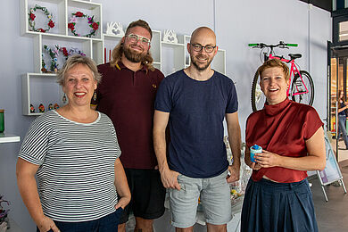 Gruppenbild in der Elsterkammer mit Karin Leonhardt, Tom Spindler, Frank Braun und Susann Rüthrich (v.l.) Dahinter Regaler mit Produkten und an der Wand ein pinkes Fahrrad 