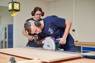 Ein Teilnehmer sägt ein Stück Holz und trägt Gehörschutz