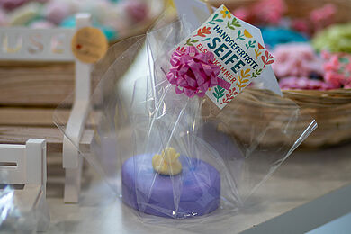 In transparenter Plastikfolie verpackte lila Seife mit kleinem Produktschild und der Aufschrift "Handgefertigte Seife"