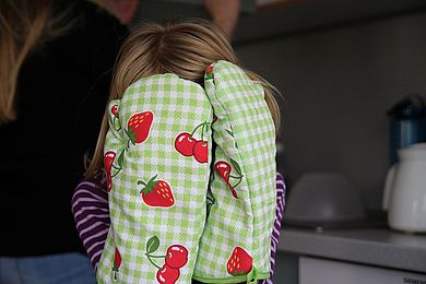 Mädchen mit Backhandschuhen versteckt sein Gesicht.