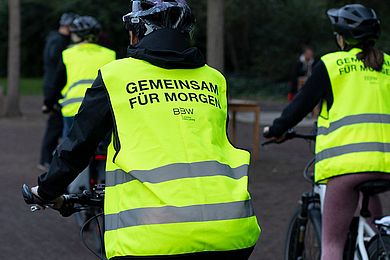 Radfahrende Person mit Warnweste mit Schriftzug "Gemeinsam für Morgen"