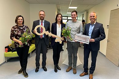 Von links nach rechts: Ines Naumann (stellvertretende Geschäftsbereichsleiterin Kindertagesstätten) mit einem Blumenstrauß in den Händen, Tobias Schmidt (Hauptgeschäftsführer der BBW-Leipzig-Gruppe) und Vicki Felthaus (Bürgermeisterin und Beigeordnete für Jugend, Schule und Demokratie) halten einen großen Holzschlüssel, David Grießmann (Leiter Integrative Kindertageseinrichtung Geschwister-Steinhausen-Straße) mit einem Blumenstrauß in den Händen und Carsten Brückner (Volks- und Raiffeisenbank Muldental eG ) mit einem Scheck in Höhe von 1000 Euro