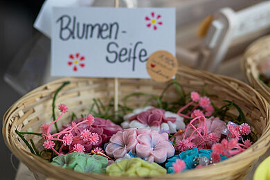 Handgefertigte Seife in Blumenform in einer Vielzahl von Farben, elegant präsentiert in einem geflochtenen Korb.