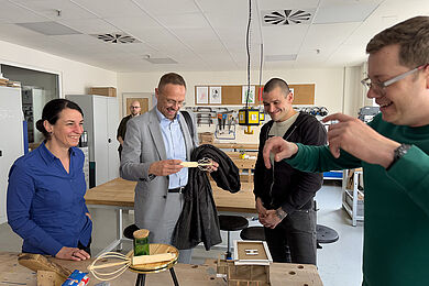 4 Personen stehen an einer Werkbank und unterhalten sich über die ausgestellten Produkte.